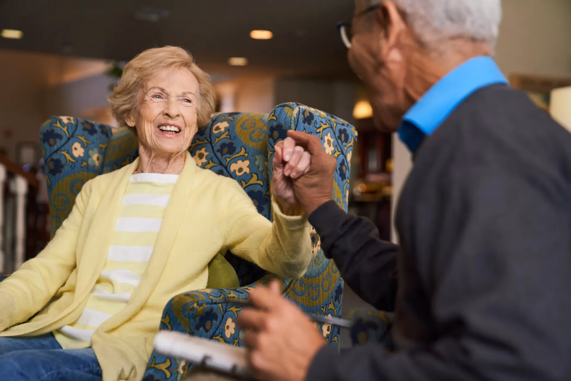Two senior residents holding hands and laughing together in the community lounge