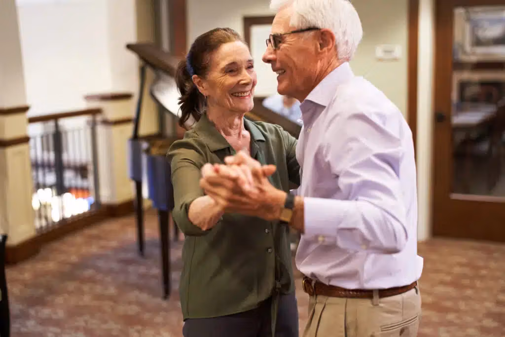 Elderly couple dancing happily indoors.