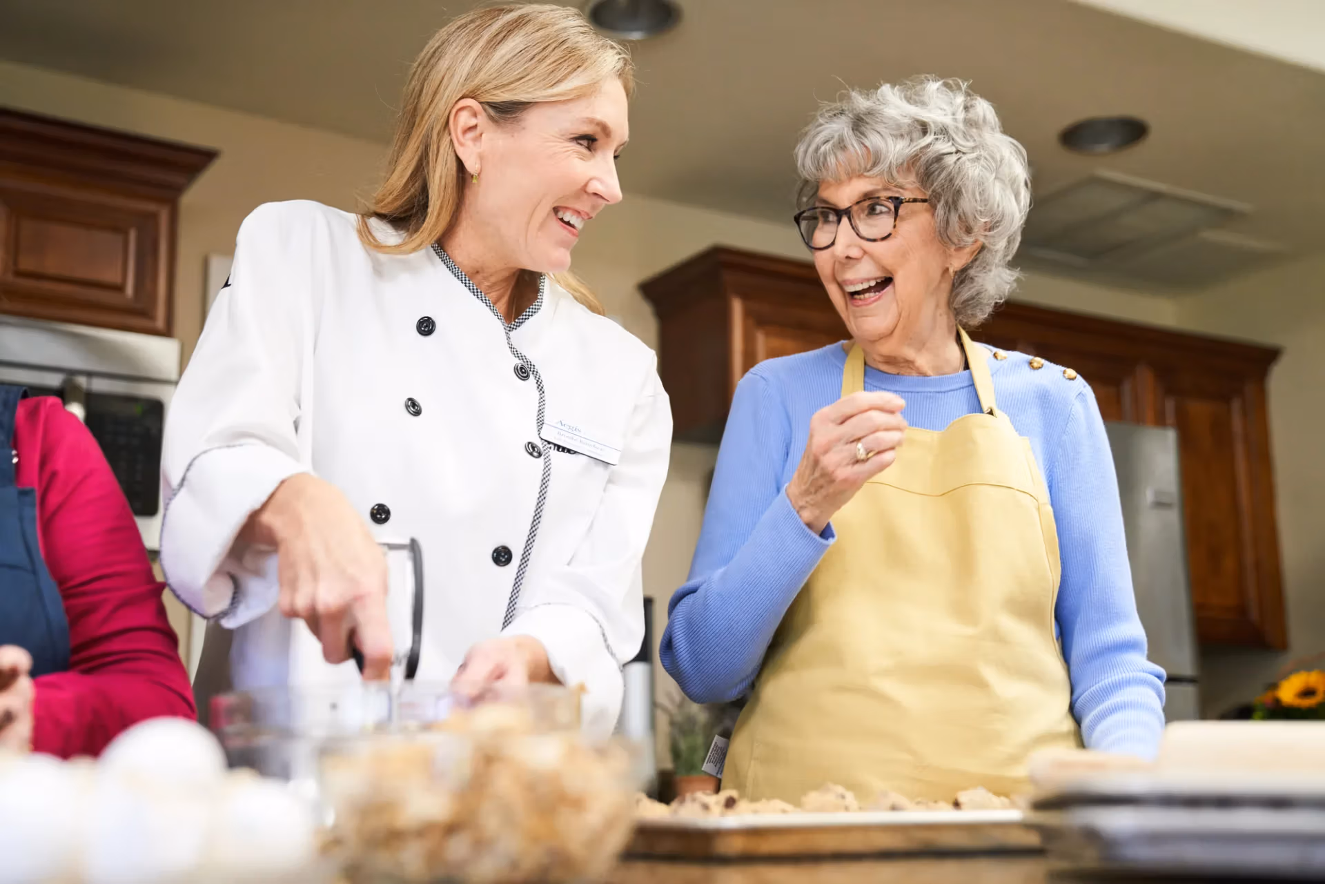 A resident and chef laughing together during a community cooking class