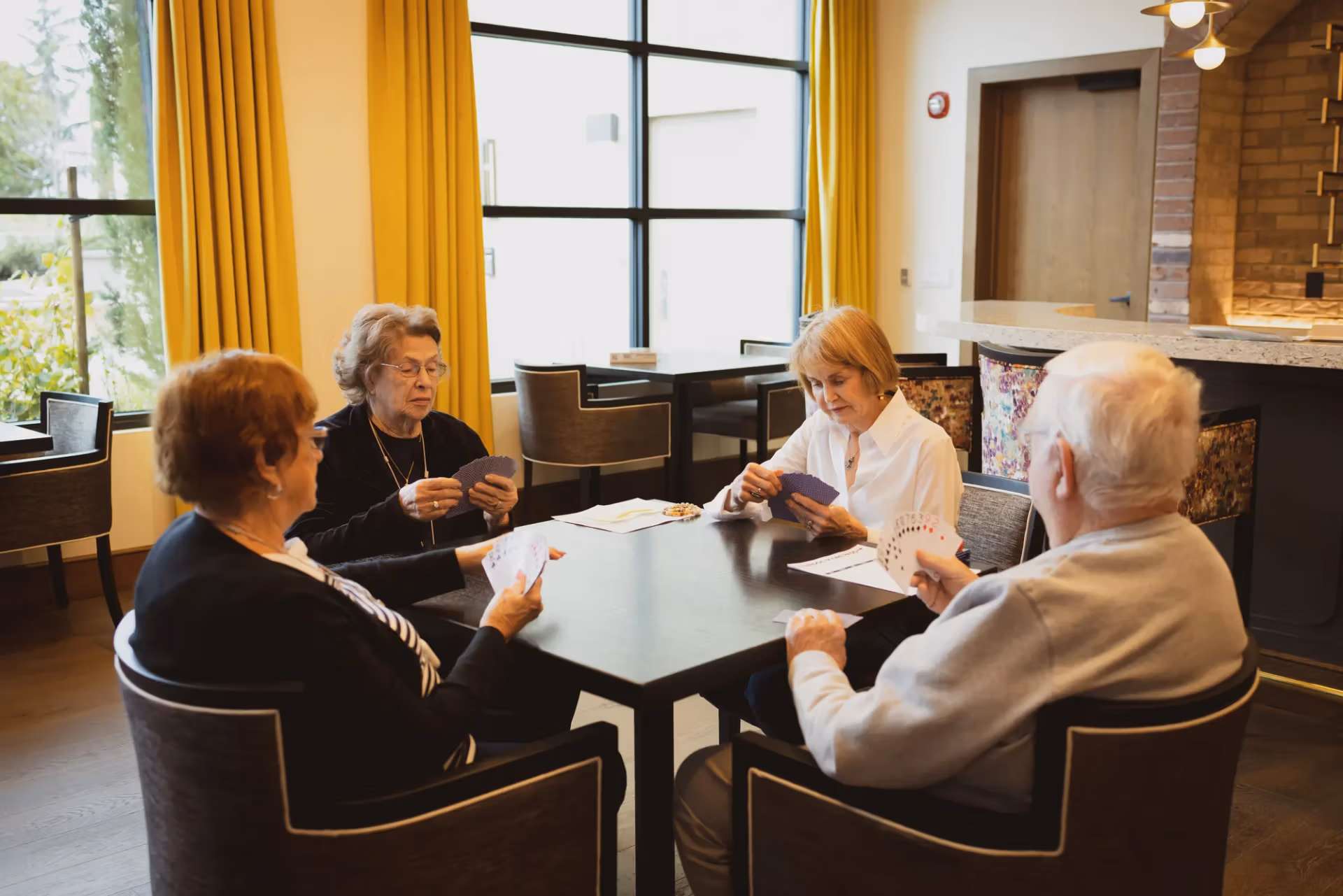 Four residents staying sharp and connected over a card game in the lounge