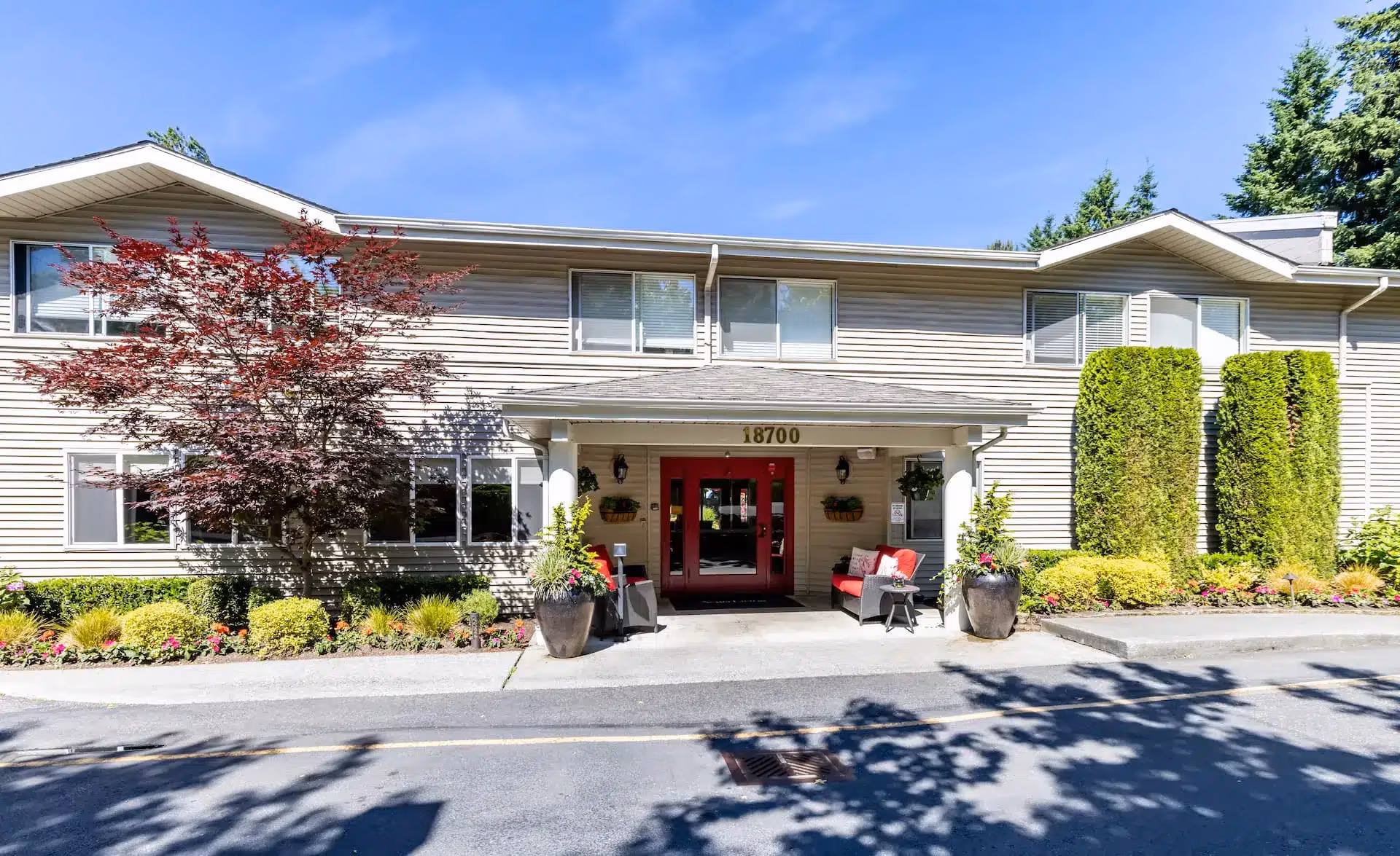 An older woman and her adult daughter smile together over tea in a sunlit Áegis Living memory care in Mukilteo, WA neighborhood with a caregiver nearby.