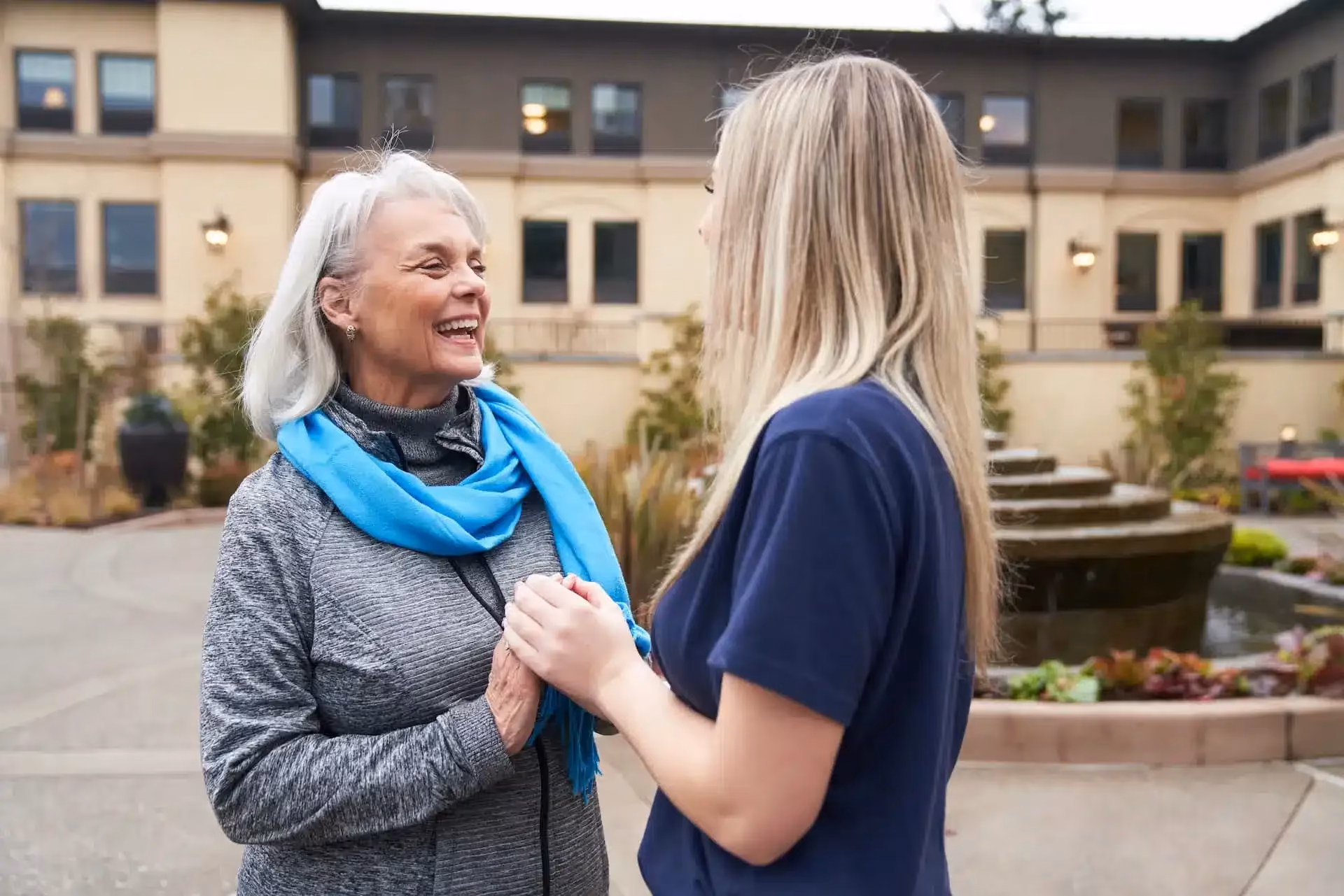 Two women smiling and talking together in an Áegis Living community courtyard