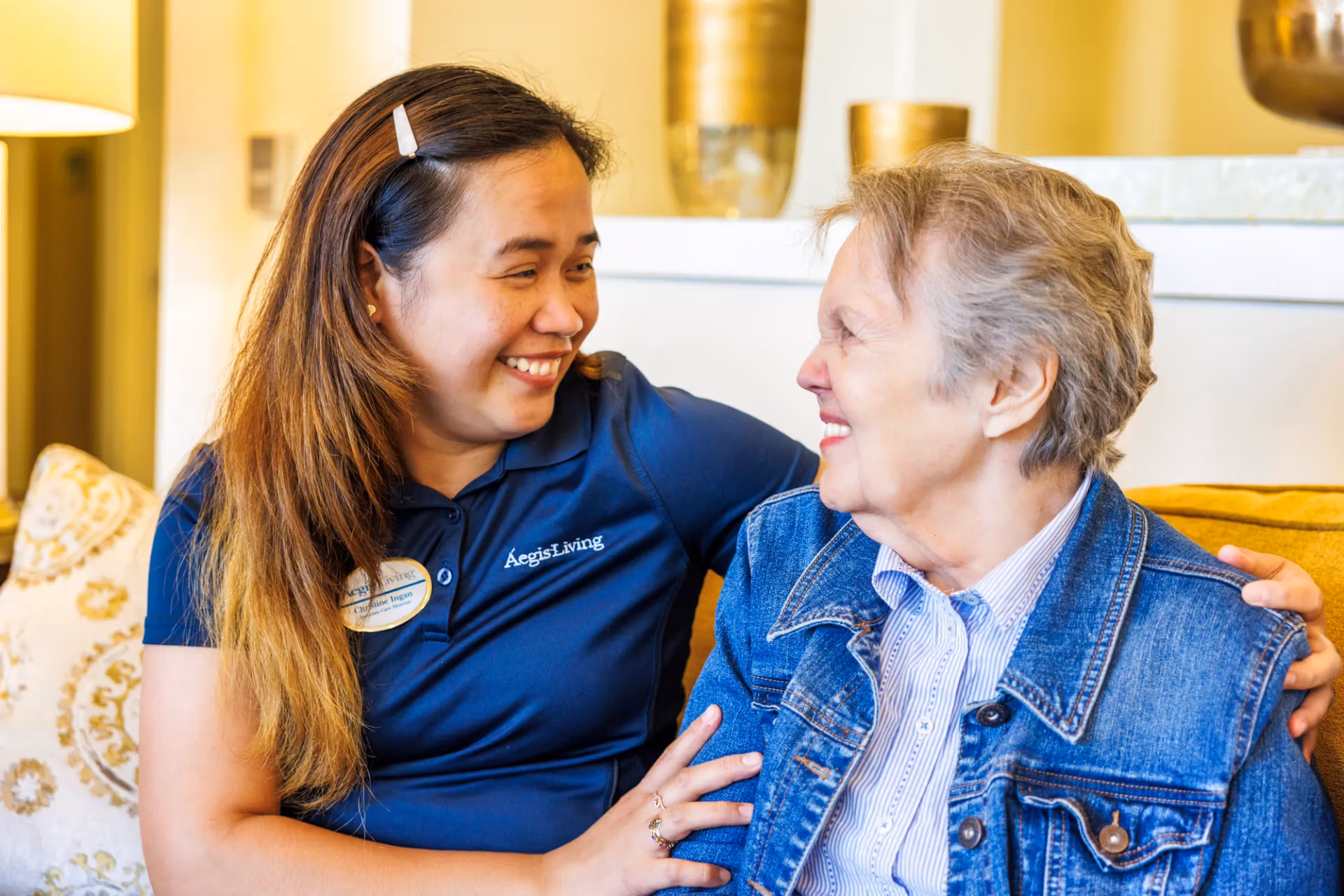 A caregiver and resident laughing together at home on the couch