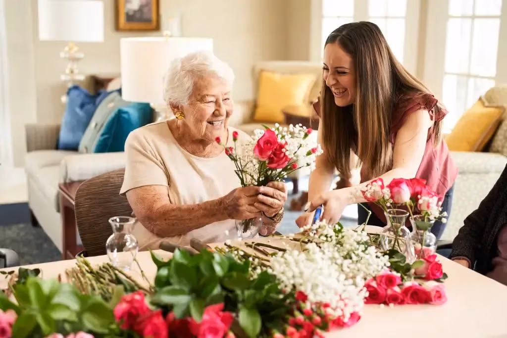 A resident and an Áegis Living team member arranging fresh flowers together in a sunlit community lounge