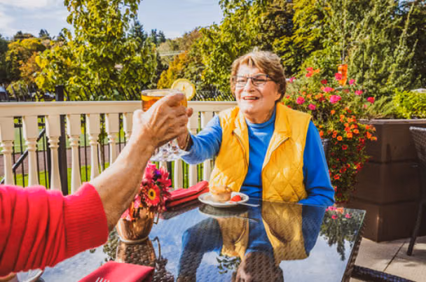 A resident toasting with iced tea on a sunny Áegis Living patio