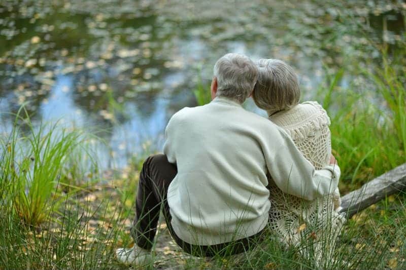 elderly couple sitting on a log looking over a lake enjoying the view