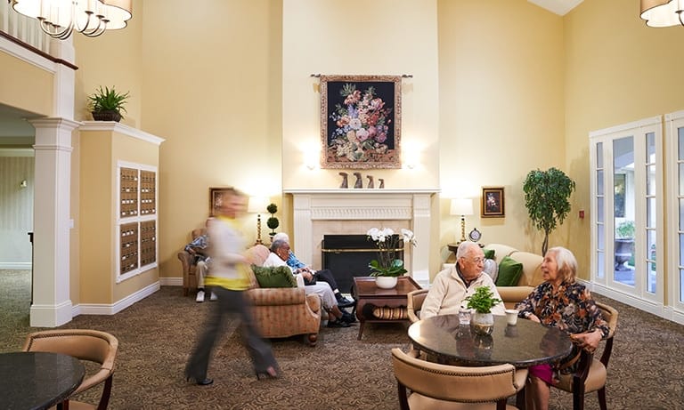 Residents sitting and talking in a tall lobby lounge with a fireplace, mailboxes, and armchairs