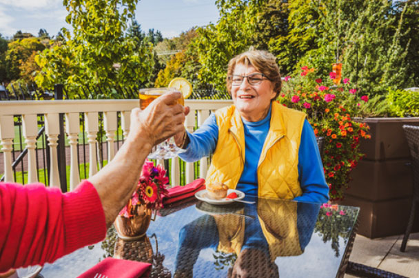 A resident toasting with iced tea on a sunny Áegis Living patio